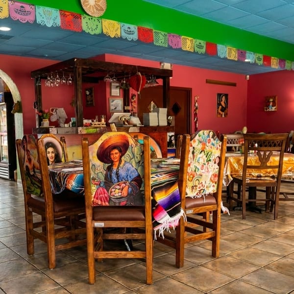 Vibrant Mexican restaurant interior with colorful chairs, papel picado, and festive decor.