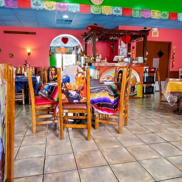 Vibrant Mexican restaurant interior with colorful decor, painted chairs, and serape-covered tables.