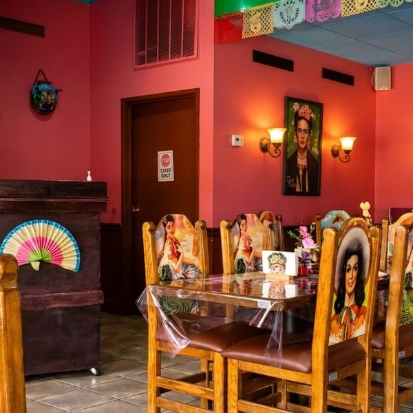 Vibrant Mexican restaurant interior with pink walls, colorful chairs, and Frida Kahlo artwork.