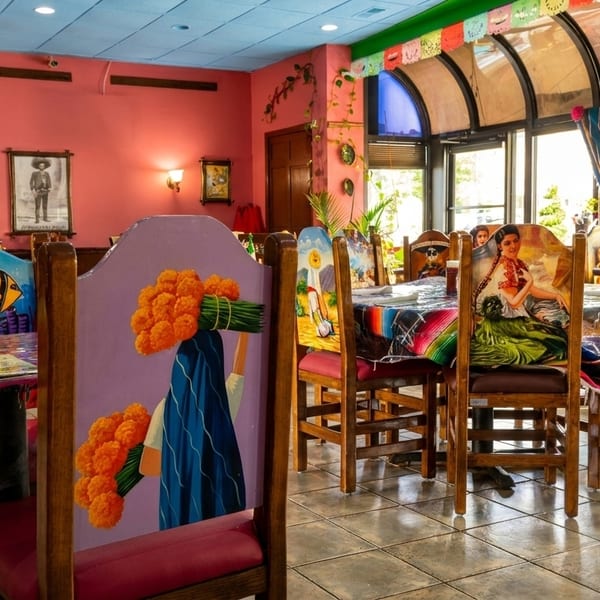 Vibrant Mexican restaurant interior with colorful murals, painted chairs, and festive decorations.