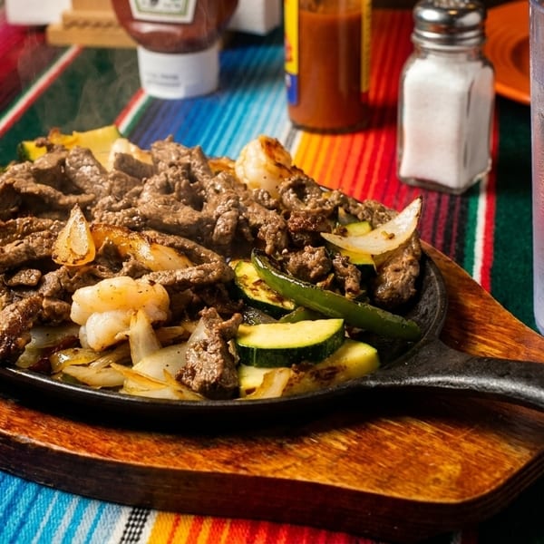 Sizzling fajitas with steak, shrimp, onions, zucchini, and peppers in a cast iron skillet.