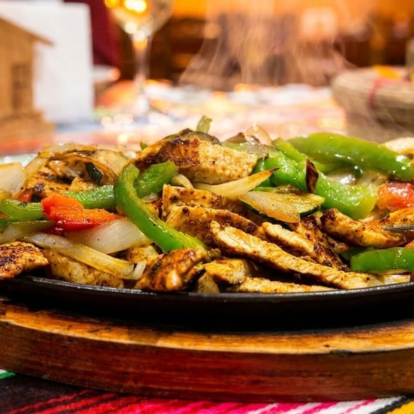 Sizzling chicken fajitas with colorful bell peppers and onions on a wooden platter.