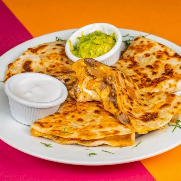 Cheesy quesadillas with beef, served with guacamole and sour cream on a white plate.